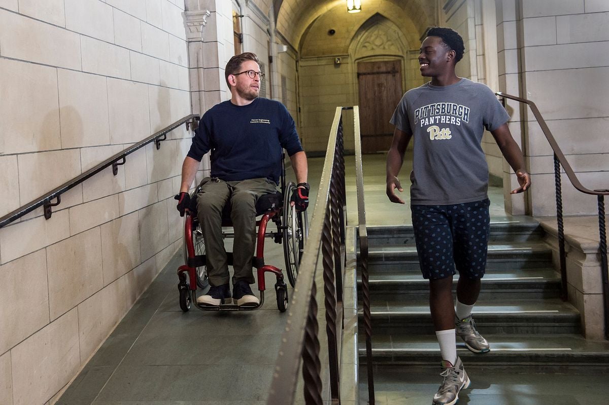 File photo: Students Aaron Anderson, left, and Glenn Ayieko, demonstrate accessibility improvements around the Cathedral of Learning, Aug. 14, 2018.