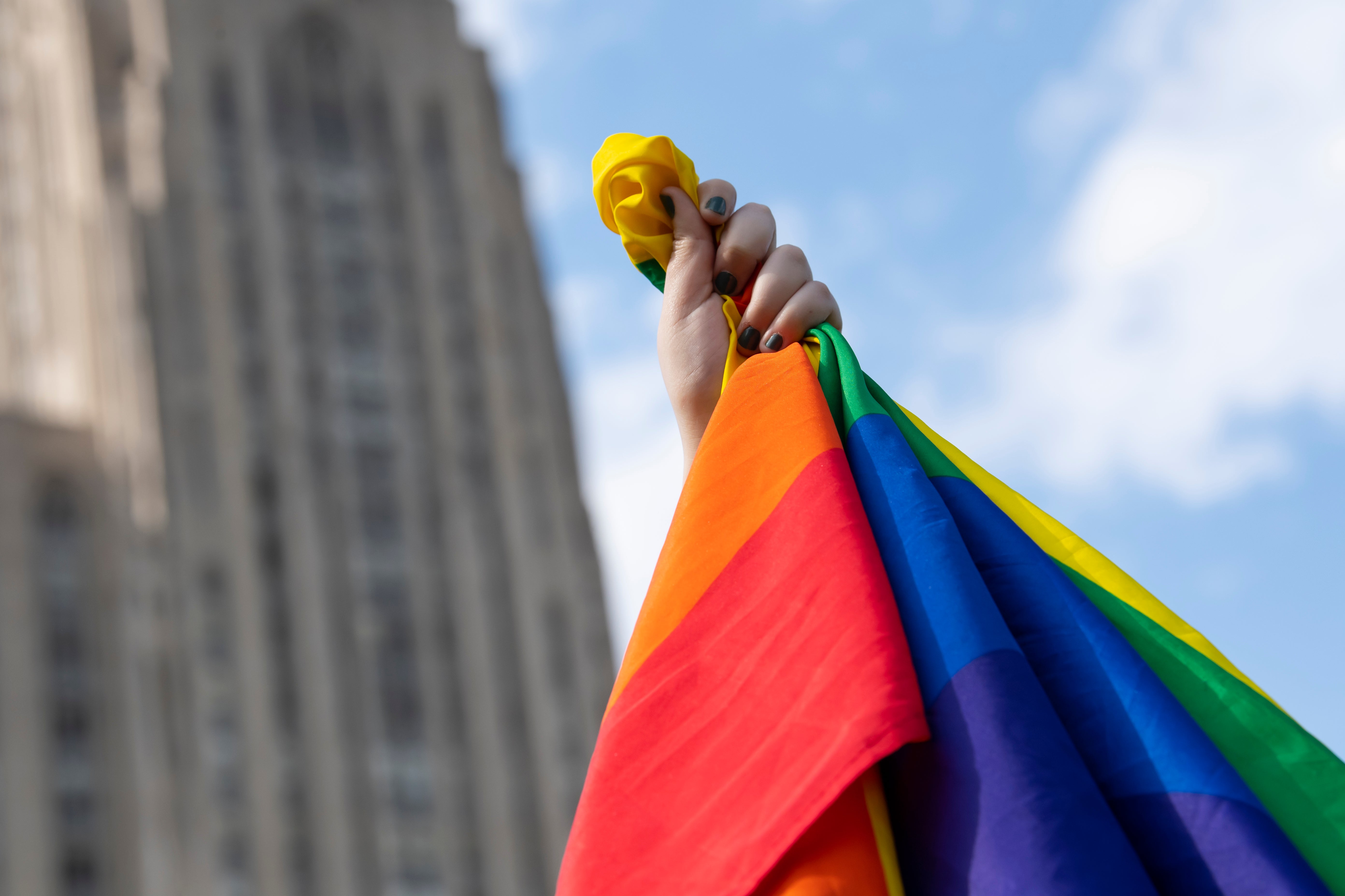 LGBTQIA+ Pride Flag held in a fist in front of the Cathedral of Learning