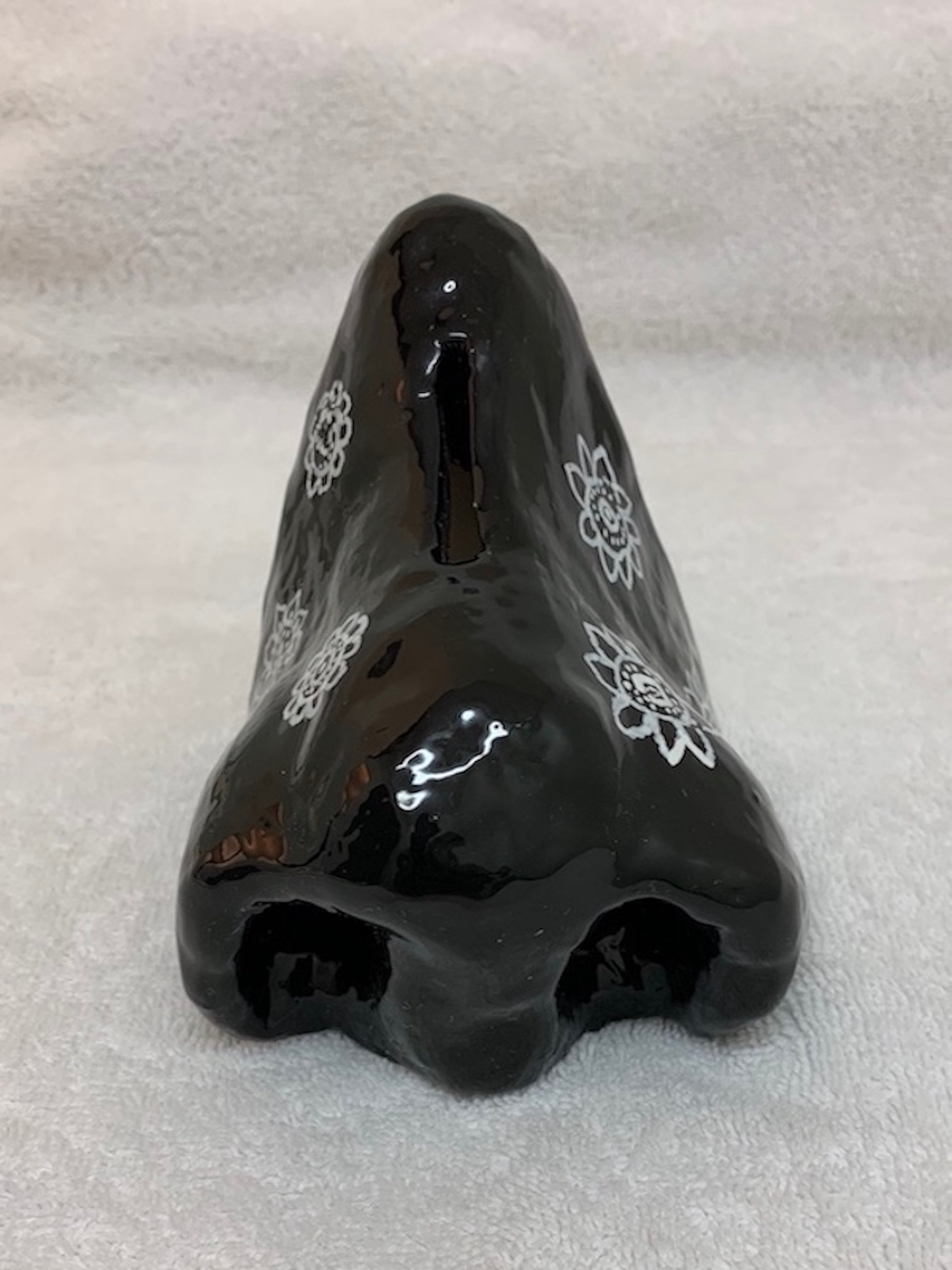a ceramic sculpture of a black nose decorated with four white floral-like designs