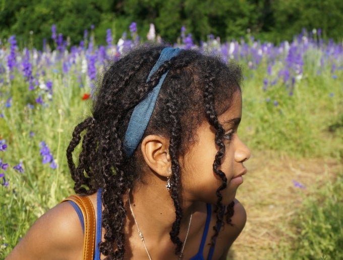 photograph of a young Black girl looking to the right. She is in a field with purple flowers
