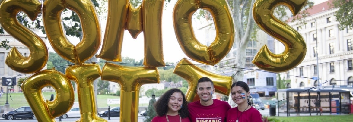 Pitt students in front of Somos Pitt balloons